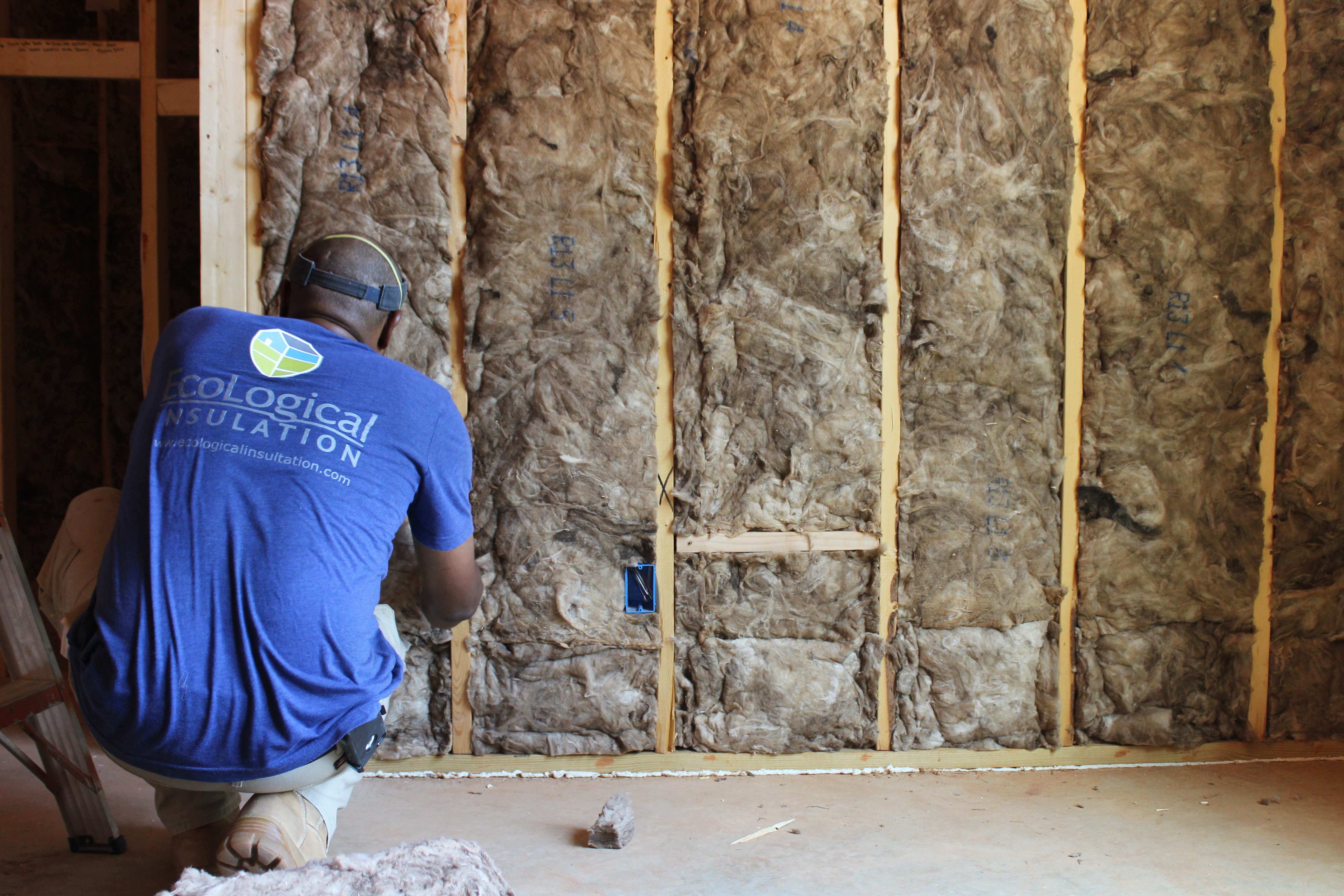 man installing fiberglass insulation in a wall cavity